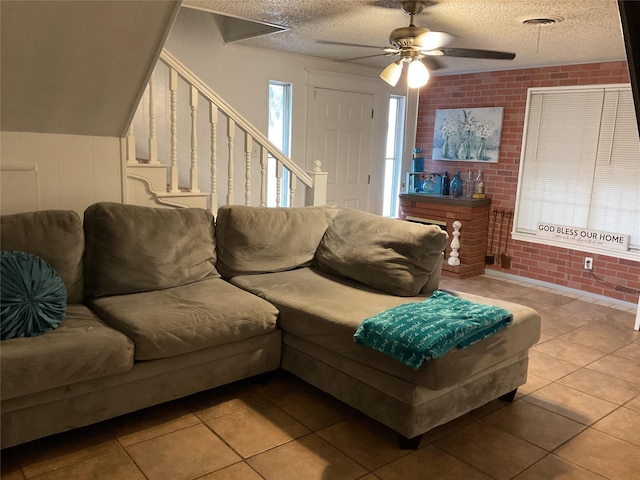 living room with ceiling fan, light tile patterned flooring, brick wall, and a textured ceiling