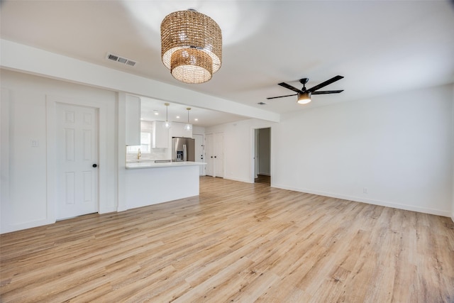 unfurnished living room featuring ceiling fan with notable chandelier and light hardwood / wood-style flooring