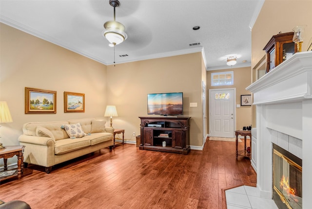 living room featuring hardwood / wood-style flooring, ceiling fan, ornamental molding, and a tiled fireplace