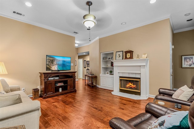 living room with hardwood / wood-style floors, ceiling fan, crown molding, and a tile fireplace