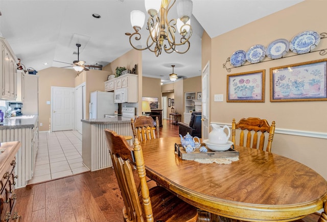 dining space with ceiling fan with notable chandelier, light wood-type flooring, and vaulted ceiling