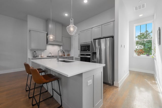 kitchen featuring light hardwood / wood-style flooring, stainless steel appliances, an island with sink, tasteful backsplash, and sink