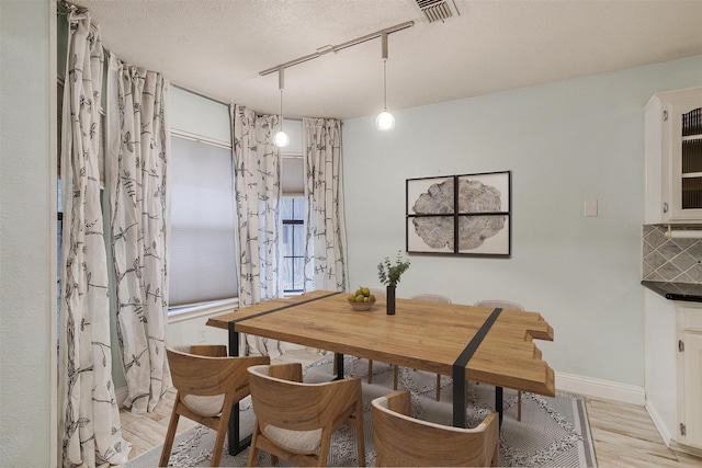 dining room with a textured ceiling, visible vents, baseboards, light wood-style floors, and track lighting