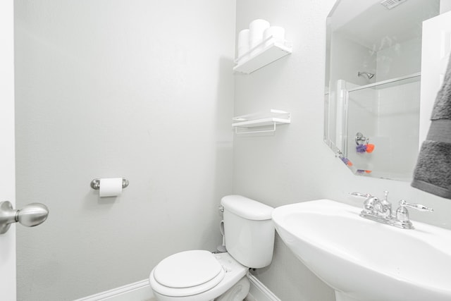 bathroom featuring toilet, a shower with door, and sink