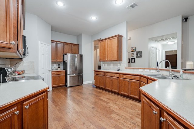 kitchen featuring sink, light wood-type flooring, stainless steel appliances, and backsplash