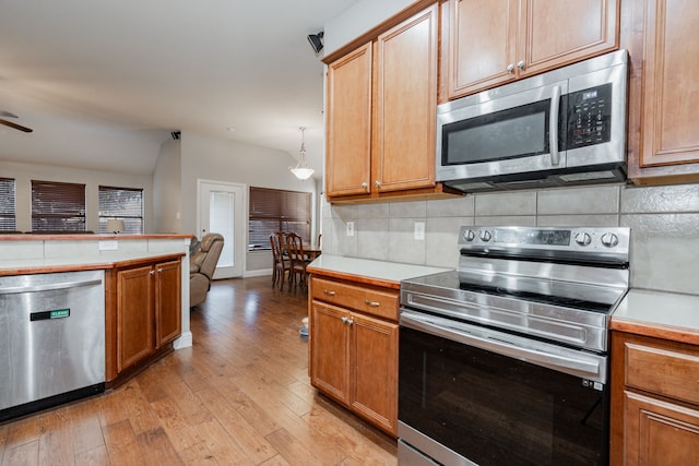 kitchen featuring decorative backsplash, light hardwood / wood-style flooring, pendant lighting, and appliances with stainless steel finishes