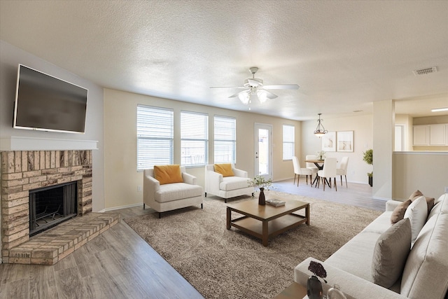 living room with ceiling fan, a fireplace, wood-type flooring, and a textured ceiling