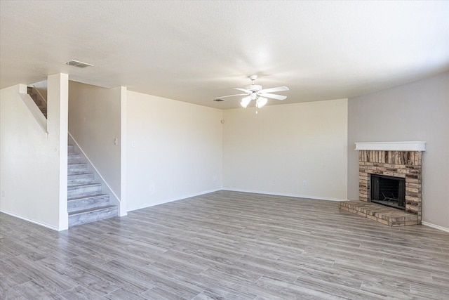 unfurnished living room featuring ceiling fan, light hardwood / wood-style flooring, a textured ceiling, and a brick fireplace