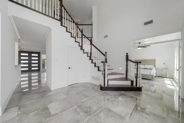 stairway with ceiling fan, a towering ceiling, ornamental molding, and french doors