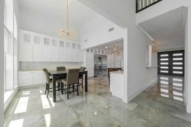 dining space featuring a notable chandelier, a towering ceiling, crown molding, and french doors