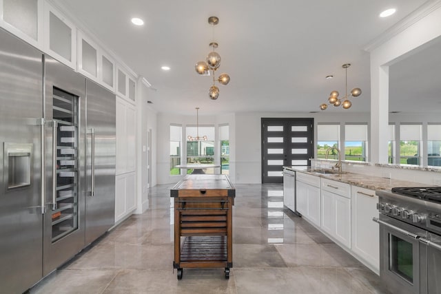 kitchen with light stone countertops, pendant lighting, premium appliances, and white cabinetry