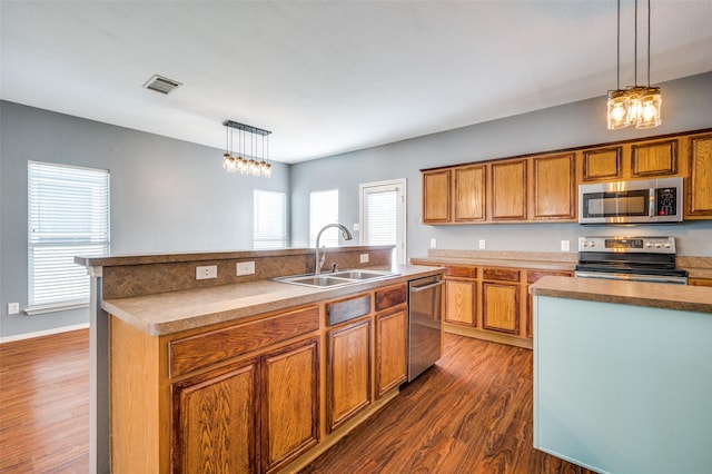 kitchen with a kitchen island with sink, sink, pendant lighting, and appliances with stainless steel finishes