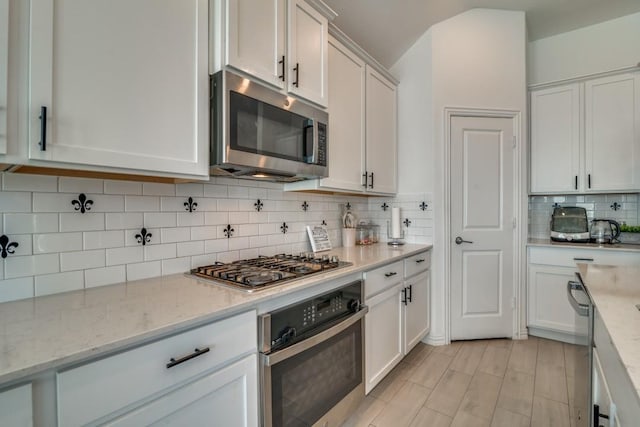 kitchen with light stone countertops, appliances with stainless steel finishes, tasteful backsplash, and white cabinetry