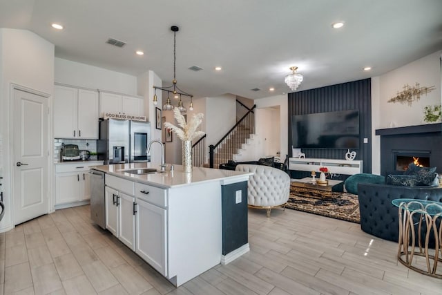 kitchen with a center island with sink, white cabinets, sink, appliances with stainless steel finishes, and a chandelier