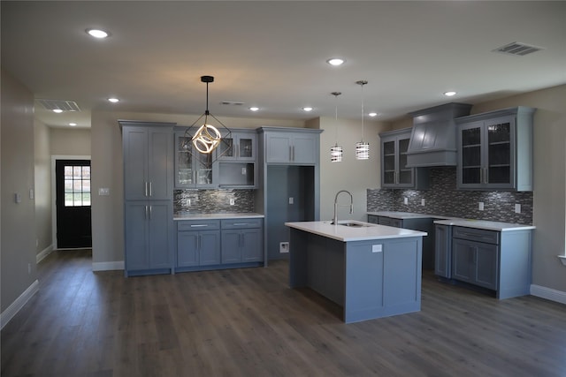 kitchen featuring sink, dark wood-type flooring, hanging light fixtures, a kitchen island with sink, and custom range hood