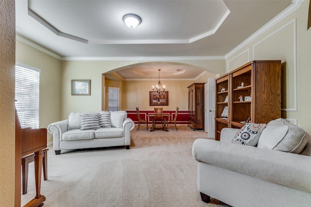 living room with light carpet, a raised ceiling, crown molding, and a notable chandelier