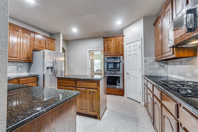 kitchen featuring light tile patterned floors, backsplash, stainless steel appliances, and dark stone counters