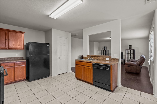 kitchen featuring dark stone counters, black appliances, sink, light hardwood / wood-style flooring, and a textured ceiling