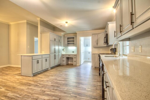 kitchen with light stone countertops, kitchen peninsula, light wood-type flooring, crown molding, and sink