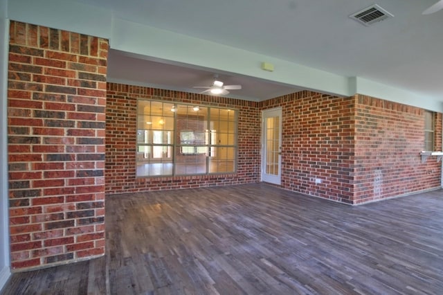 unfurnished living room featuring ceiling fan, beam ceiling, dark wood-type flooring, and brick wall