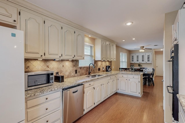 kitchen with kitchen peninsula, appliances with stainless steel finishes, ceiling fan, sink, and light hardwood / wood-style flooring