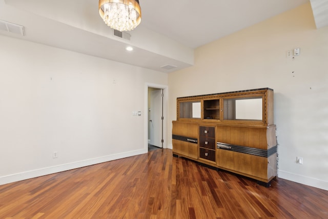 empty room with a notable chandelier and dark hardwood / wood-style floors