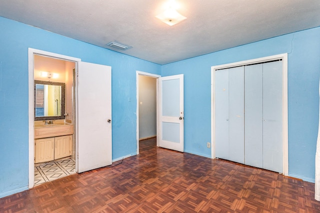 unfurnished bedroom featuring ensuite bath, sink, dark parquet floors, a textured ceiling, and a closet