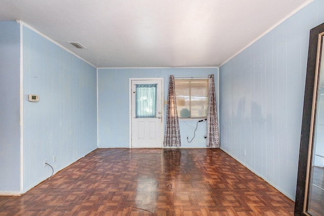 empty room featuring dark parquet flooring, ornamental molding, and wooden walls