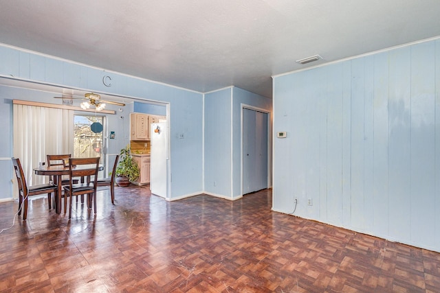 dining room with dark parquet flooring, wooden walls, and ceiling fan