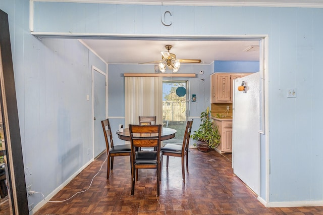 dining room featuring dark parquet flooring, ceiling fan, crown molding, and wood walls