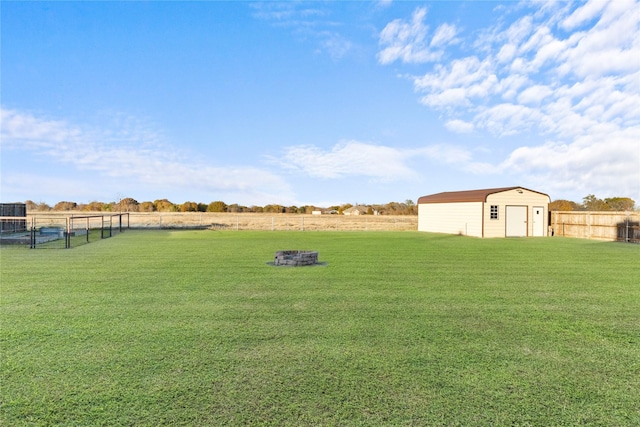 view of yard with fence, a shed, an outdoor structure, a rural view, and a fire pit
