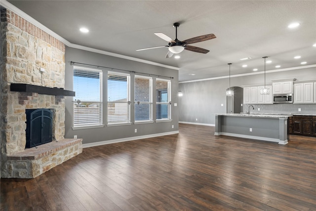 unfurnished living room featuring ornamental molding, a ceiling fan, dark wood-style floors, a stone fireplace, and baseboards