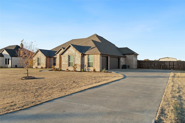 french provincial home with fence, driveway, an attached garage, central AC, and brick siding