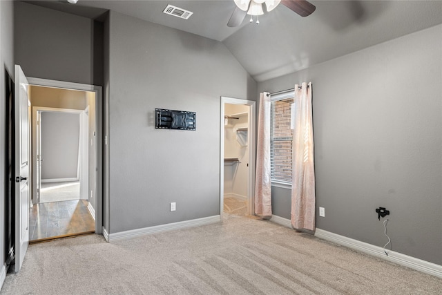 unfurnished bedroom featuring baseboards, visible vents, vaulted ceiling, a walk in closet, and carpet flooring
