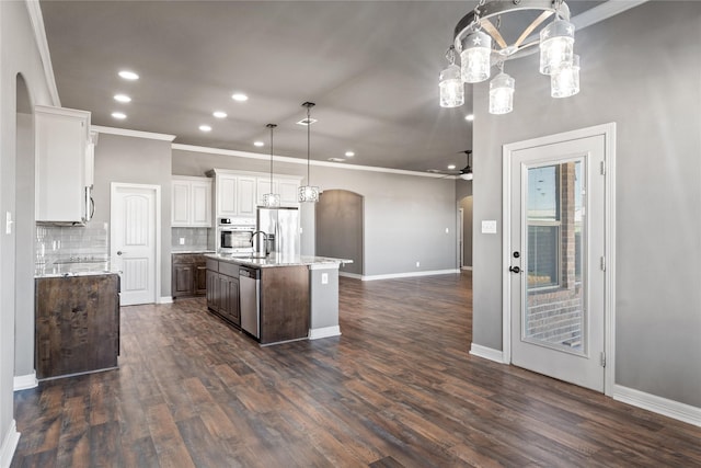 kitchen with a kitchen island with sink, white cabinets, arched walkways, and stainless steel appliances