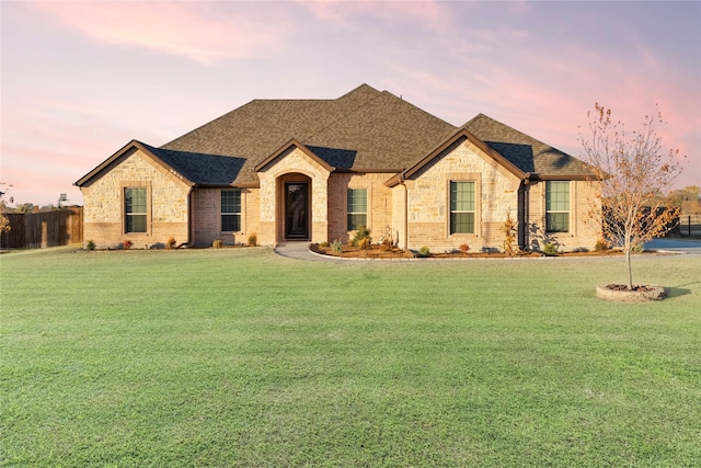 french country home with a shingled roof, a front yard, and fence