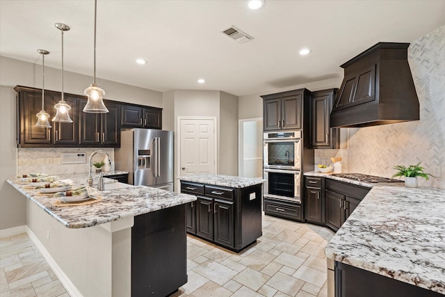 kitchen featuring custom exhaust hood, hanging light fixtures, backsplash, and appliances with stainless steel finishes