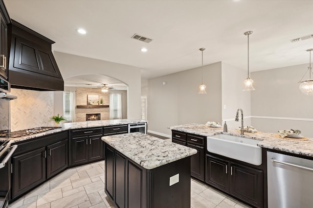 kitchen featuring ceiling fan, sink, stainless steel appliances, decorative light fixtures, and a kitchen island