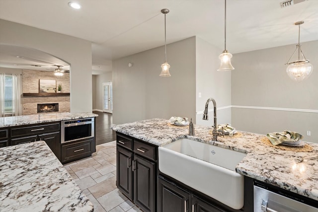 kitchen with pendant lighting, light stone counters, ceiling fan, and sink