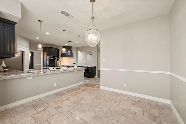 kitchen featuring stainless steel fridge, decorative light fixtures, light stone counters, and sink