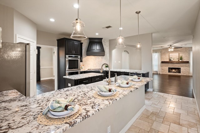 kitchen with sink, an island with sink, hanging light fixtures, and appliances with stainless steel finishes