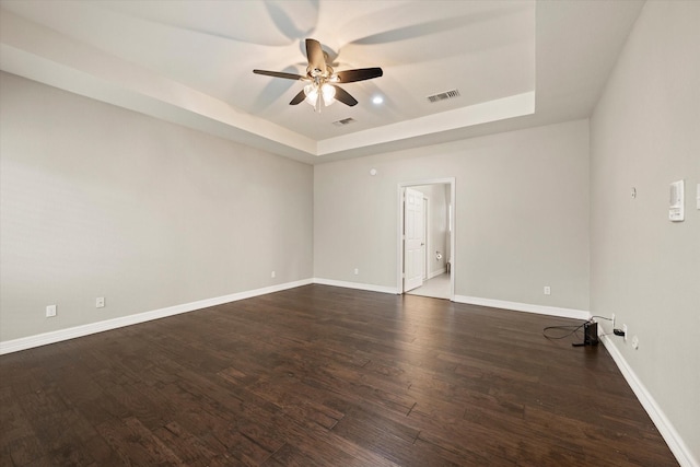 unfurnished room featuring dark hardwood / wood-style flooring, a tray ceiling, and ceiling fan