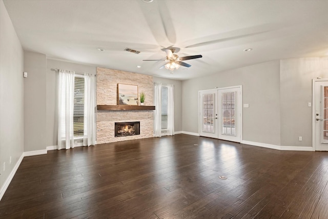 unfurnished living room with french doors, dark hardwood / wood-style flooring, a stone fireplace, and ceiling fan