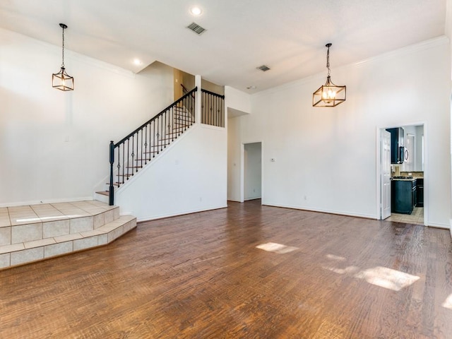 unfurnished living room with crown molding, a towering ceiling, and wood-type flooring