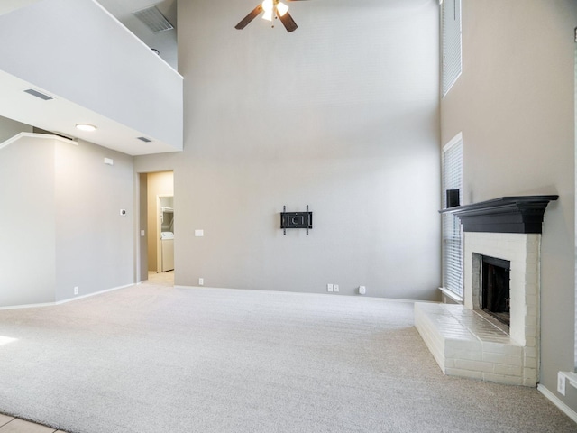 unfurnished living room featuring light carpet, a high ceiling, a brick fireplace, and ceiling fan