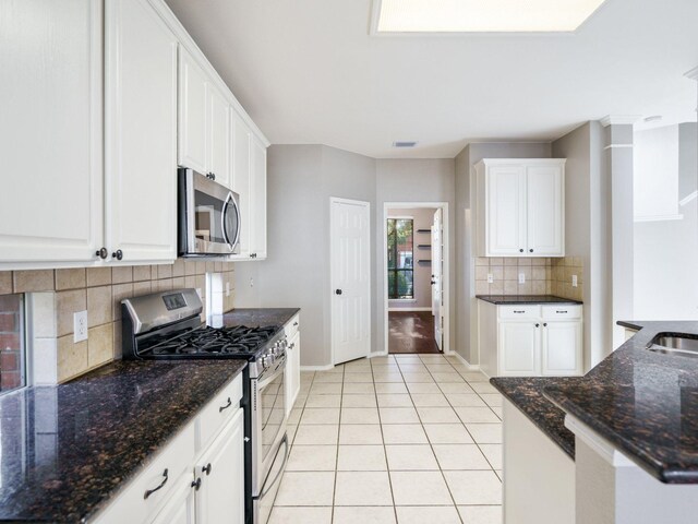 kitchen with decorative backsplash, dark stone counters, stainless steel appliances, white cabinets, and light tile patterned flooring