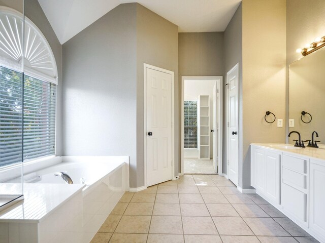 bathroom featuring tile patterned flooring, vanity, lofted ceiling, and tiled tub