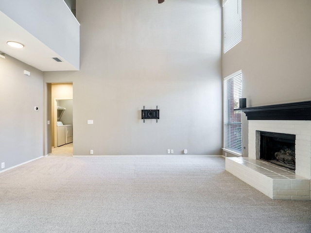 unfurnished living room featuring a brick fireplace, a towering ceiling, light colored carpet, and independent washer and dryer