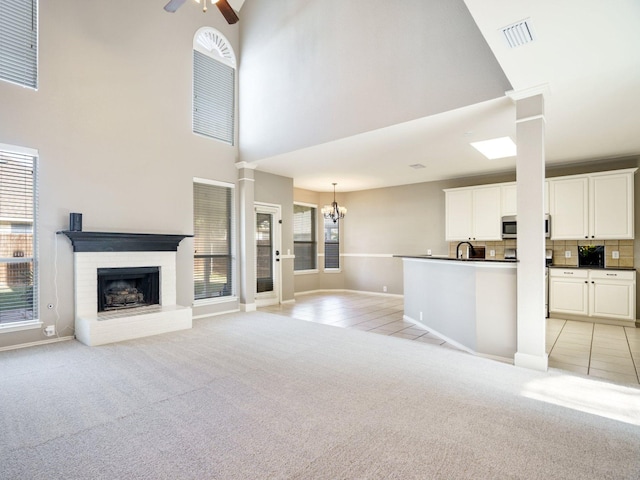 unfurnished living room featuring a fireplace, ceiling fan with notable chandelier, light colored carpet, and a high ceiling