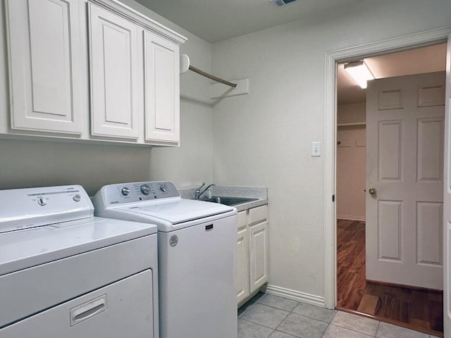 laundry room with washing machine and clothes dryer, cabinets, sink, and light hardwood / wood-style floors